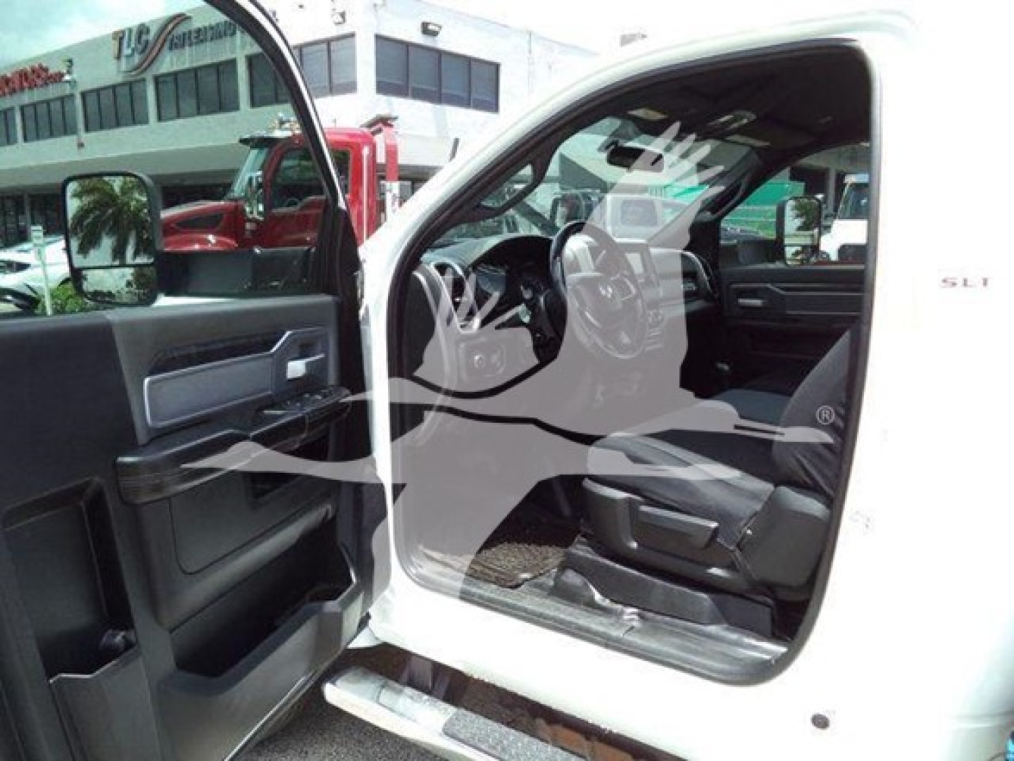 Truck cab interior of a 2021 Ram SLT with open driver door, showing the steering wheel, dashboard, and entry step; door panel and logo on the passenger side visible.