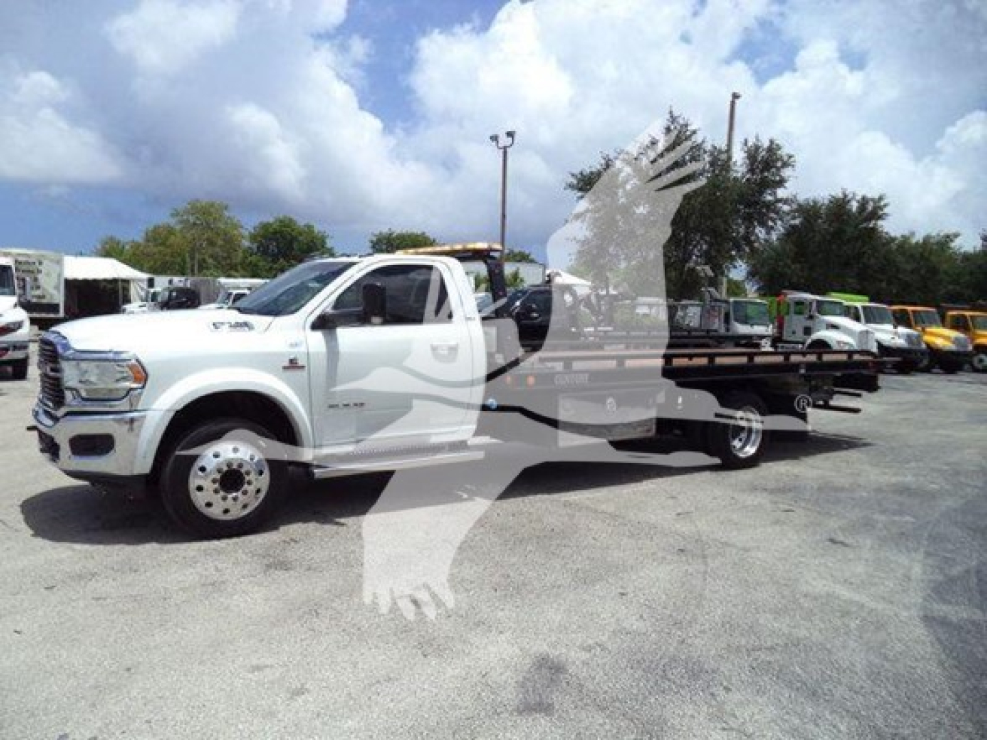 Ram pickup truck with rollback tow bed in a dealership lot, white exterior, side view showing dual rear wheel towing equipment.