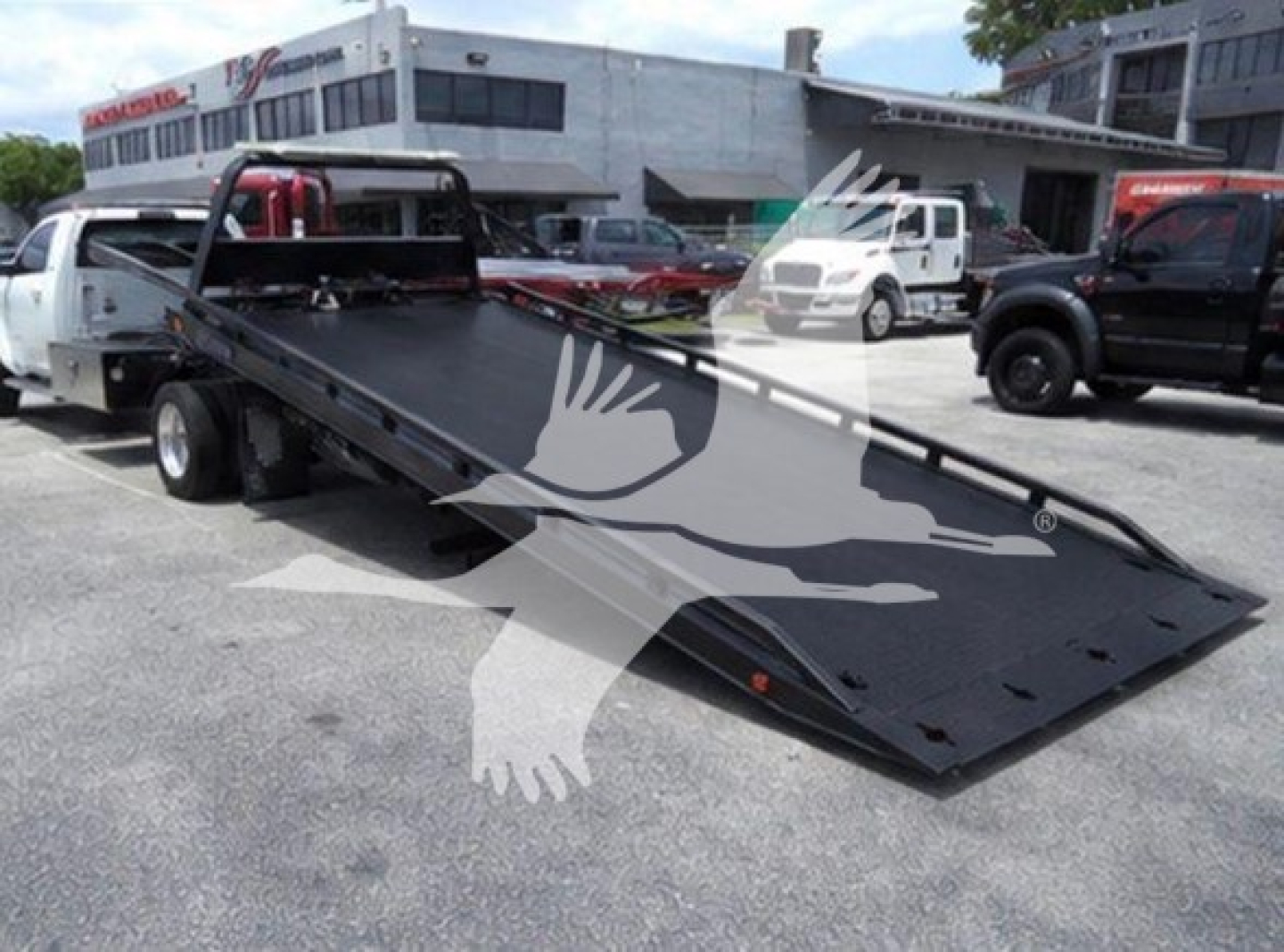 Ram tow truck rollback bed on a flatbed tow rig with hydraulic ramp and vehicle in background.