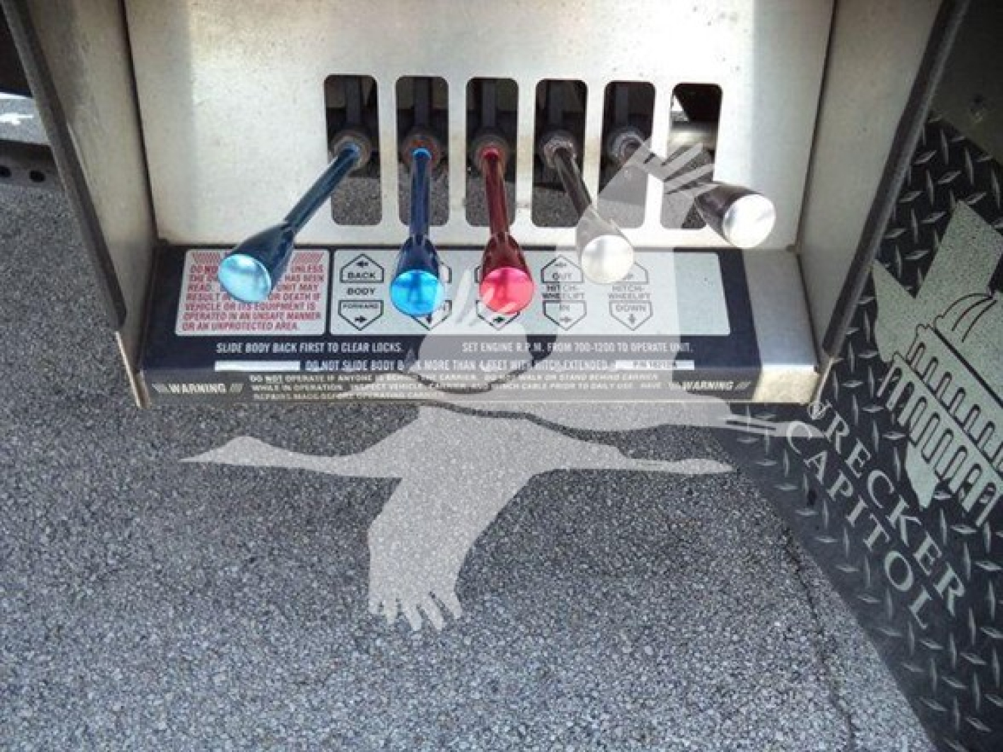 Controls and levers of a rollback tow truck selector panel with four colored levers (blue, light blue, red, white/gray) and warning labels beneath.