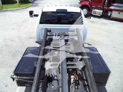 Truck bed with hydraulic rollback hoist and metal frame in view; rear of white Ram pickup with equipment storage boxes on sides and hydraulic components visible.