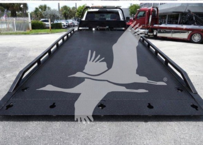 Ram pickup truck bed with a flatbed/ramp in a towing yard, visible logo watermark across the surface.