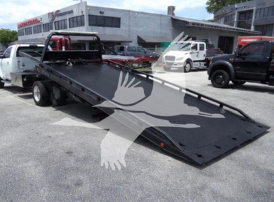 Ram tow truck rollback bed on a flatbed tow rig with hydraulic ramp and vehicle in background.