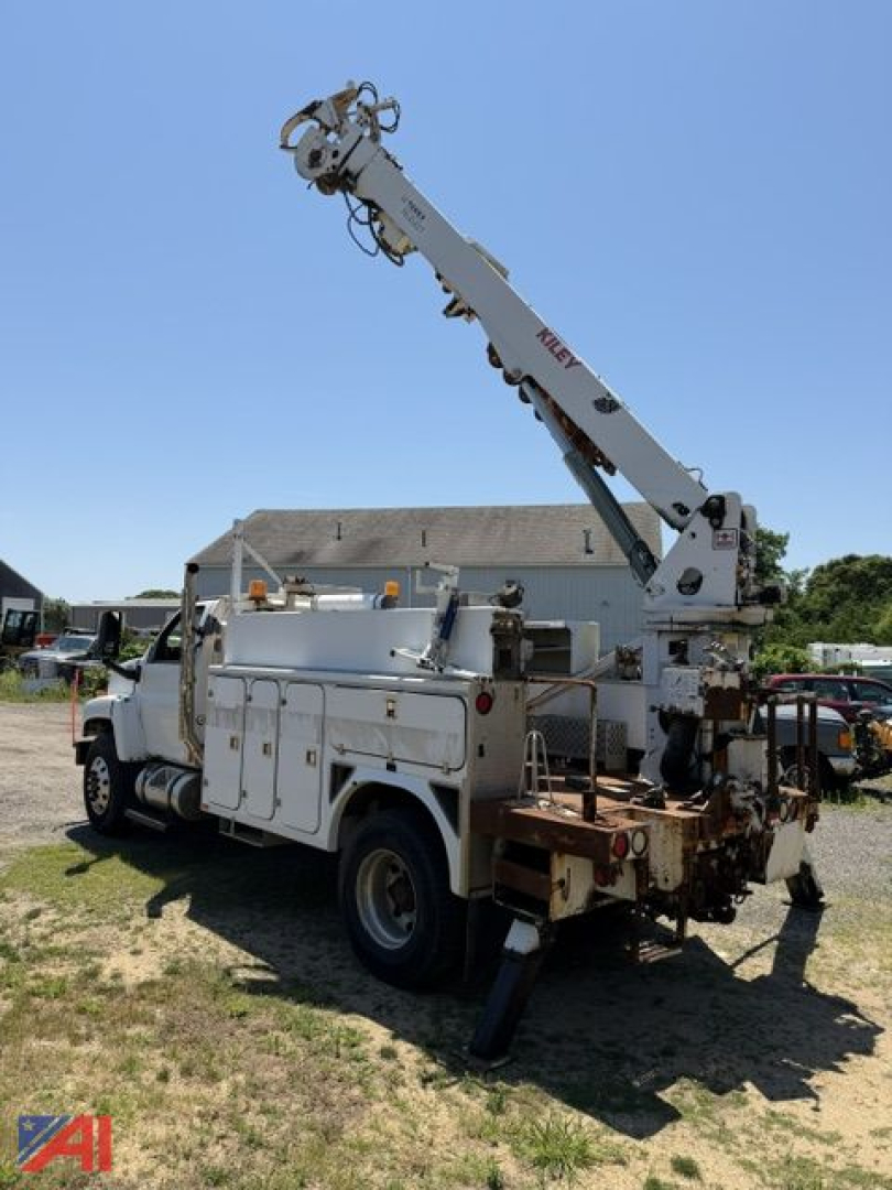 GMC C8500 digger truck with hydraulic boom extended, service compartments on side, mounted on dual rear wheels, in outdoor yard.