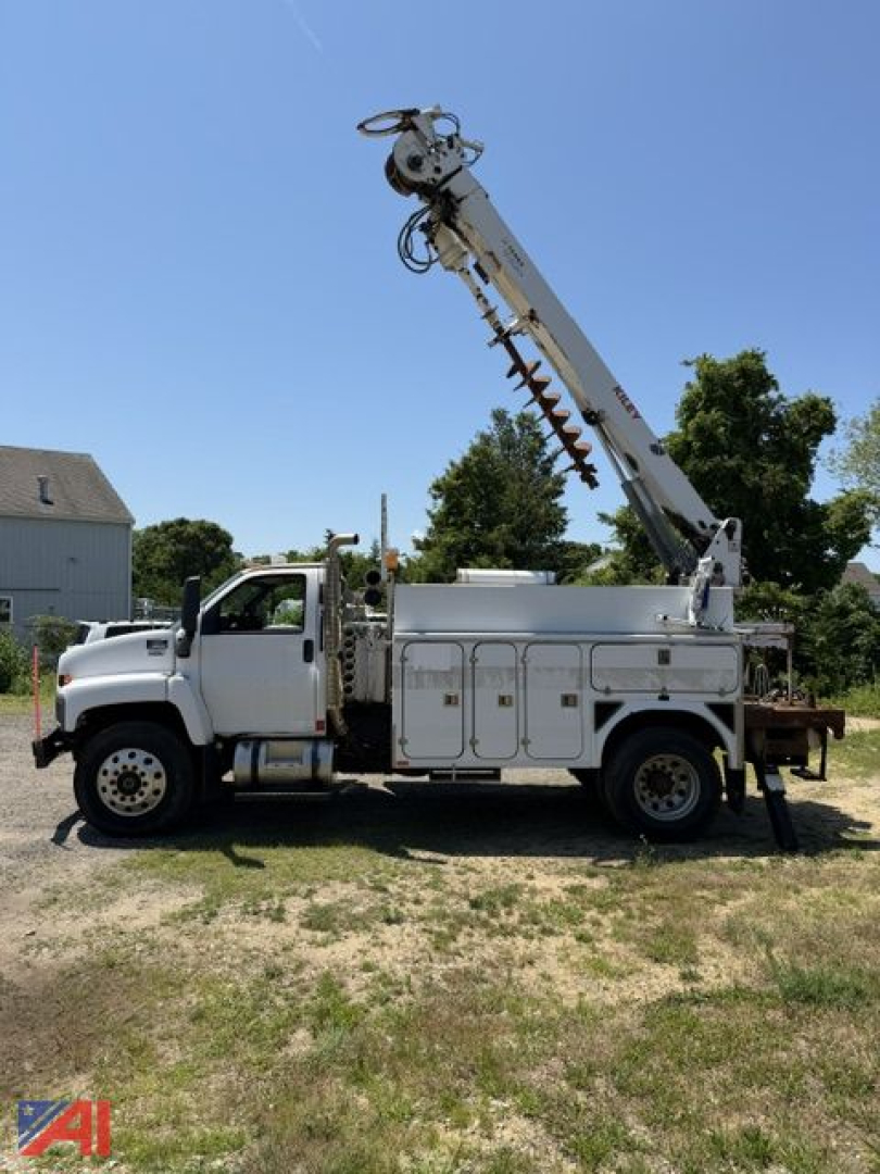 GMC C8500 digger truck side view with mounted crane and service compartments, white cab and utility bed, clear sky in background.