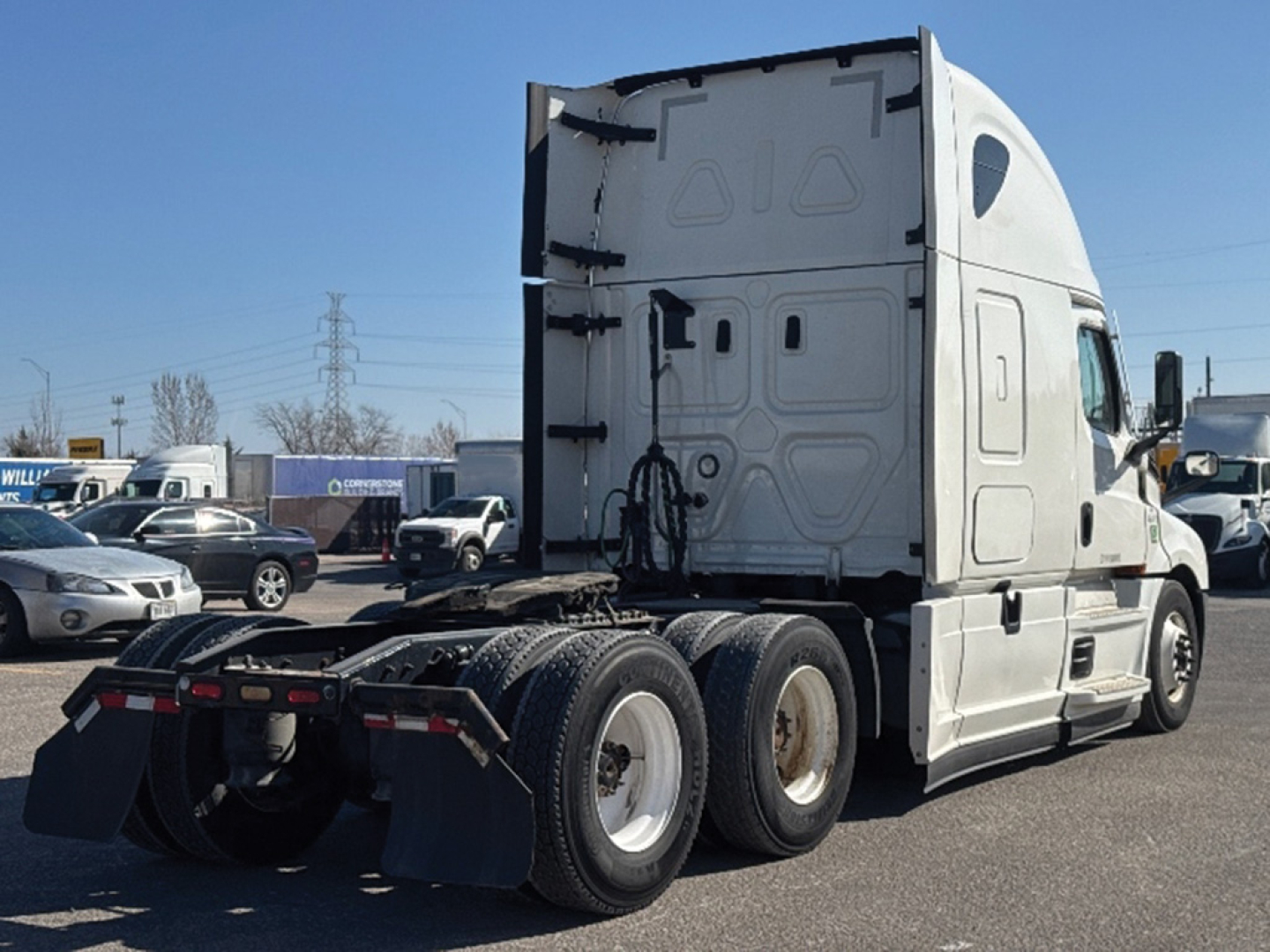 Truck cab and rear trailer wheels of a Freightliner Cascadia126 tractor showing sleeper cab, fuel tanks, and chassis with six wheels.