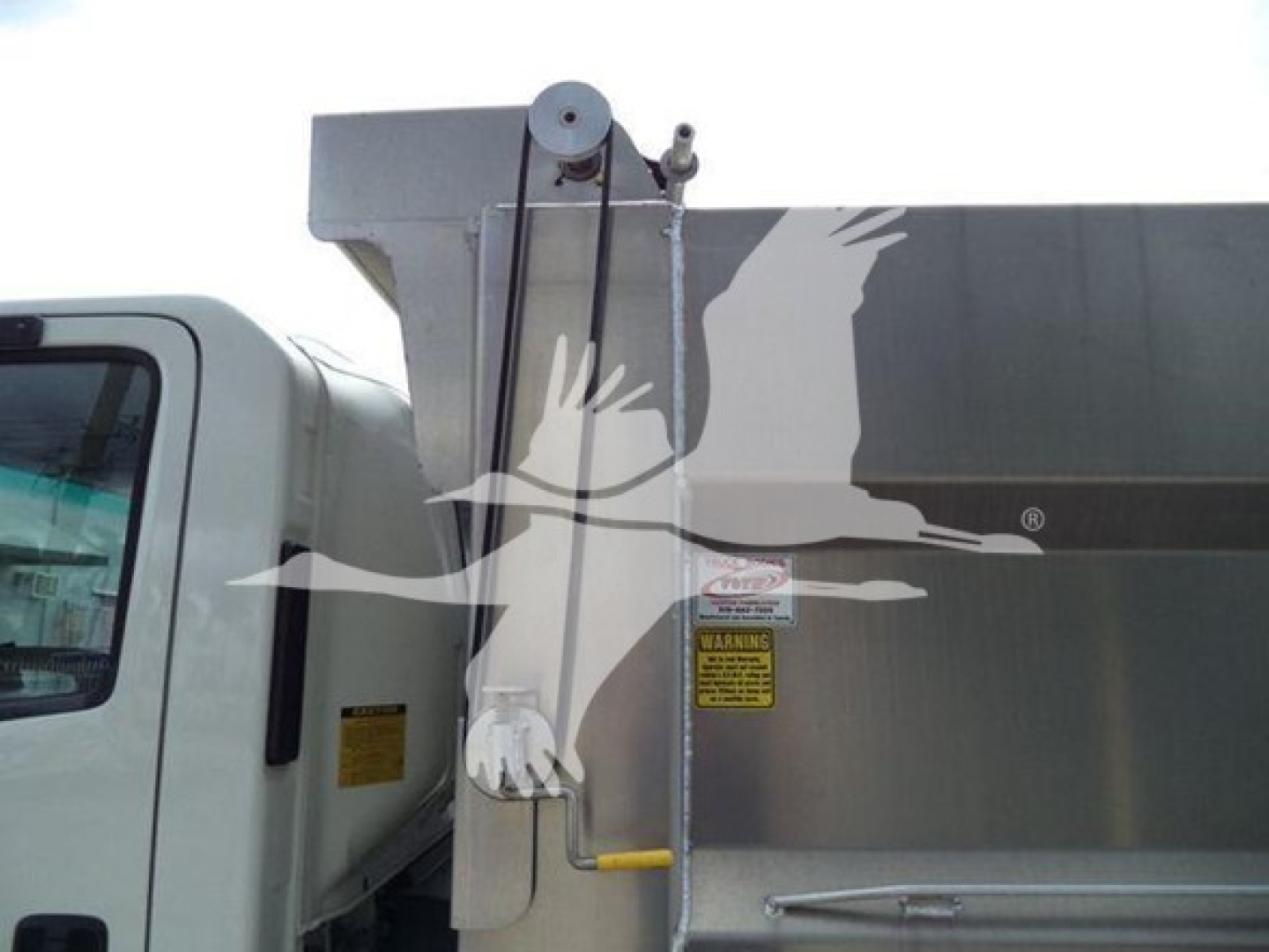 Truck side of a 2017 Chevrolet W4500 dump body showing hydraulic cylinder and warning label on metal side.