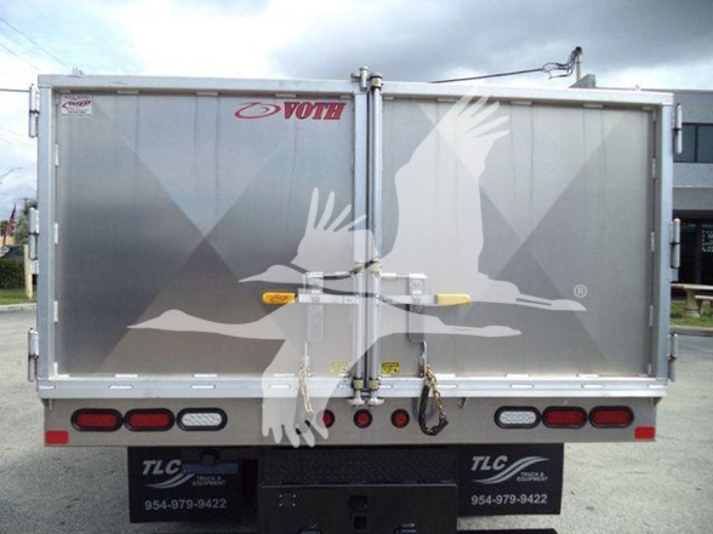 Rear view of a GMC/Chevrolet W4500 dump truck with twin barn doors featuring a large white bird graphic, VOTH brand sticker, and multiple tail lights.