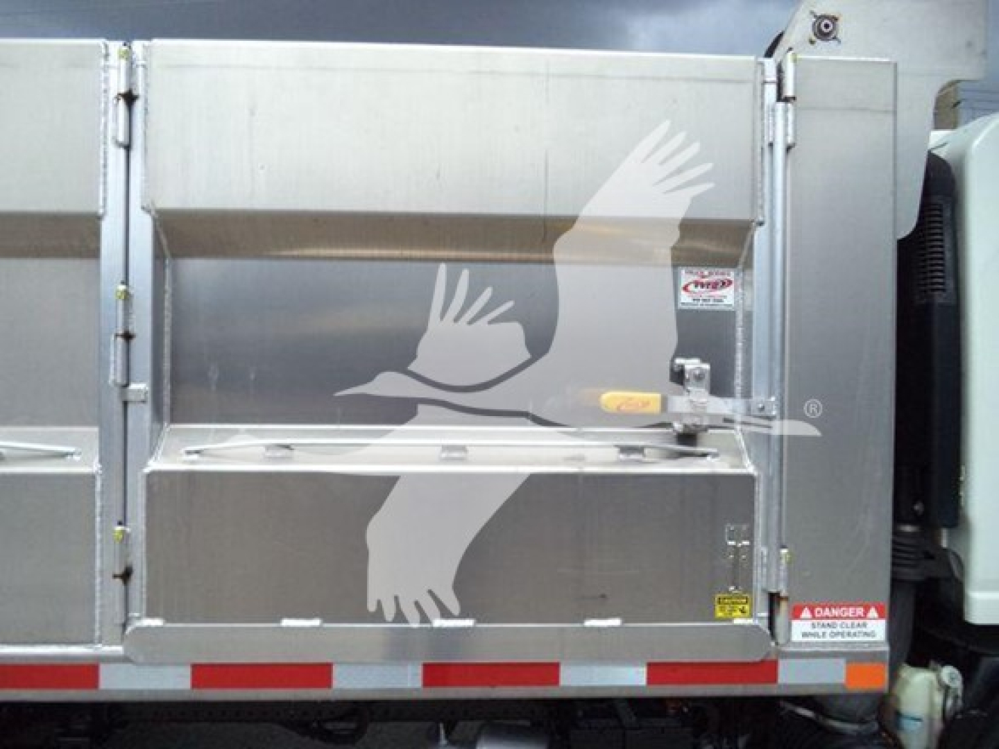 Dump truck bed showing rear tailgate with warning labels and reflective red-white stripes.