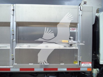 Dump truck bed showing rear tailgate with warning labels and reflective red-white stripes.