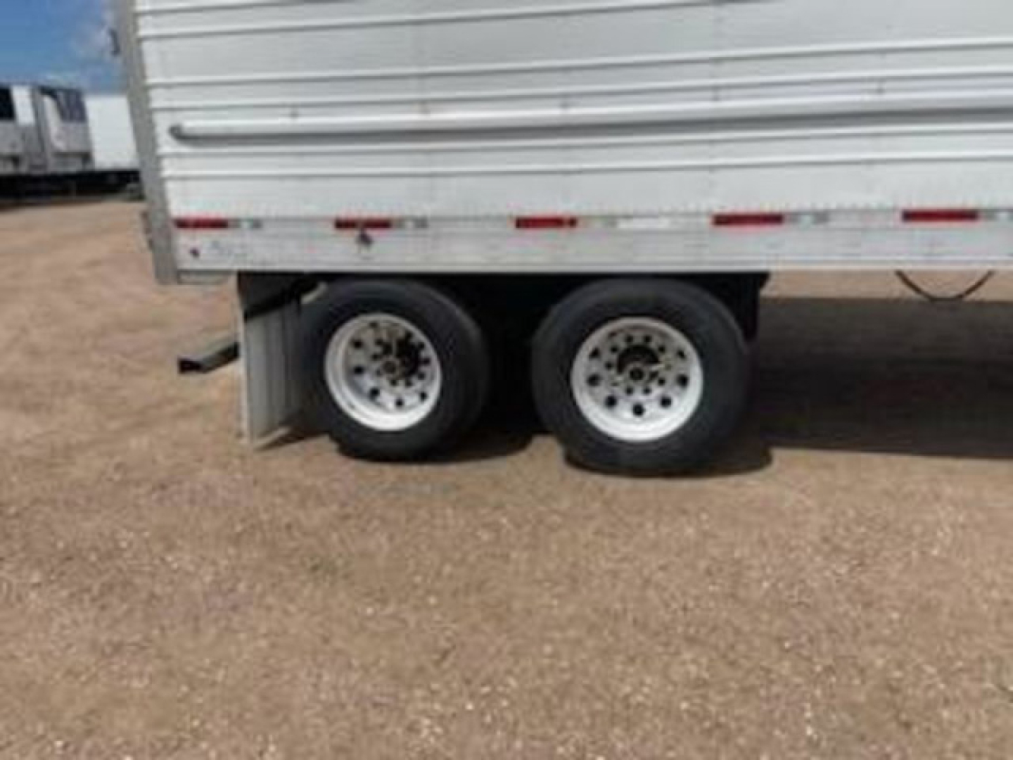 Trailer dual rear wheels on a refrigerated utility trailer with gravel ground; side panel shows no legible text.