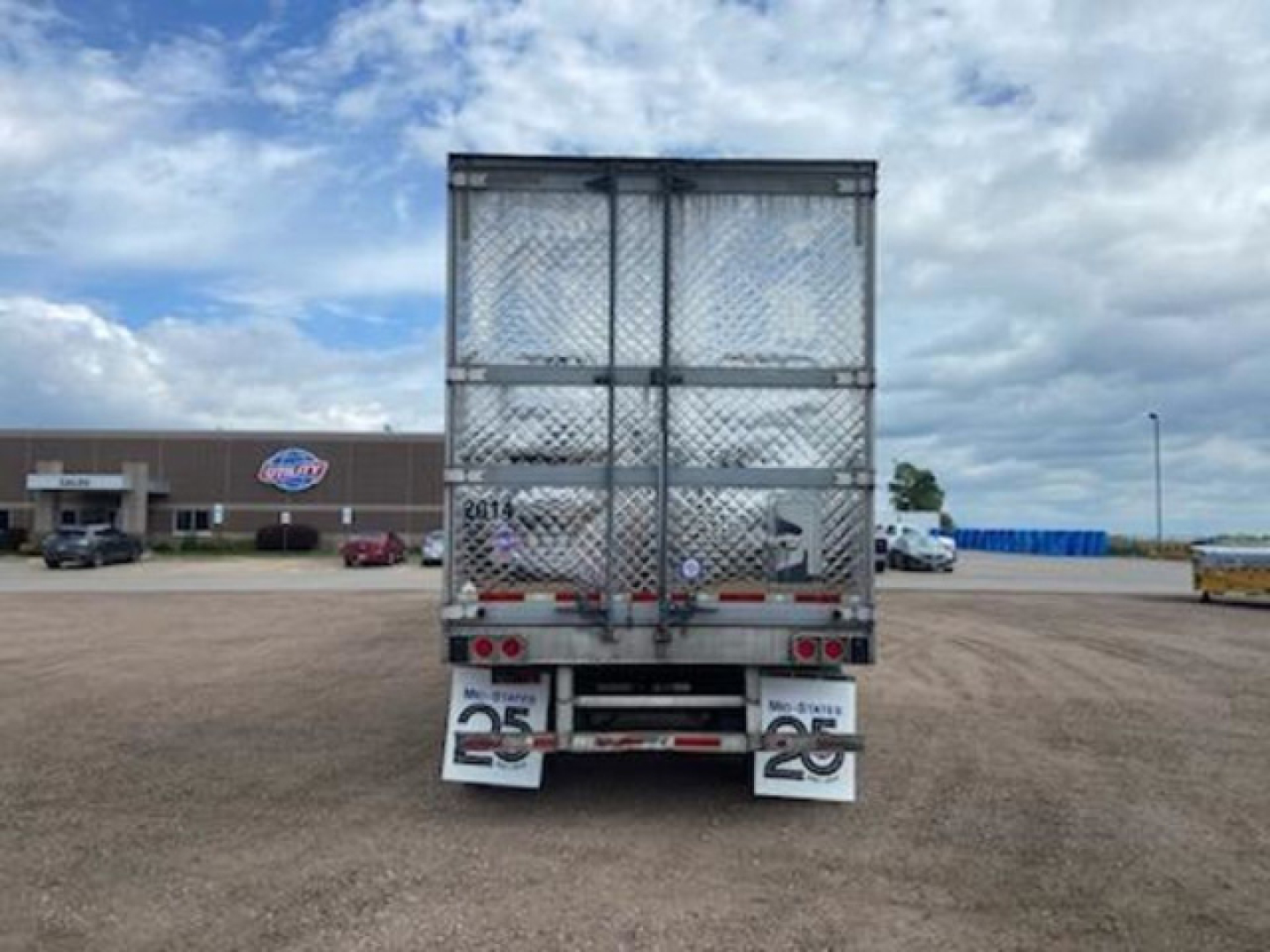 Reefer trailer rear view showing metal mesh doors, bumper with license plate area, and rear lights under a blue sky.