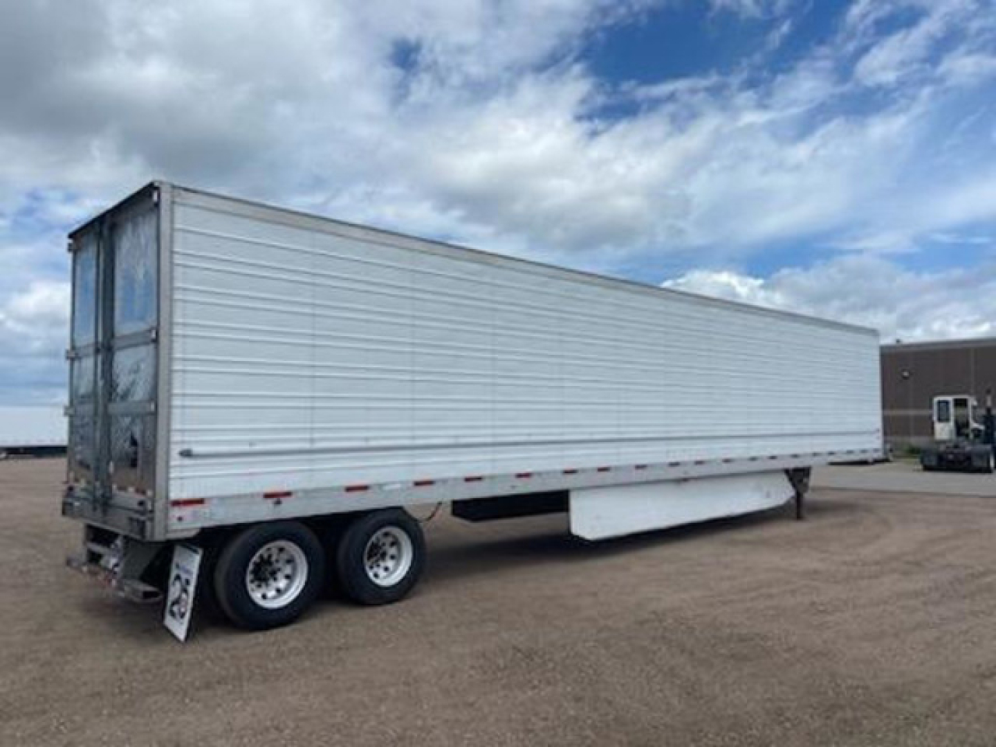Utility reefer trailer showing tandem axles and a white corrugated aluminum body with a side door closed. The rear shows reflective tape and wheel wells.