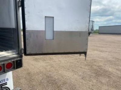 Trailer rear corner showing aluminum panel with vertical window and corner step, unloading area in background.