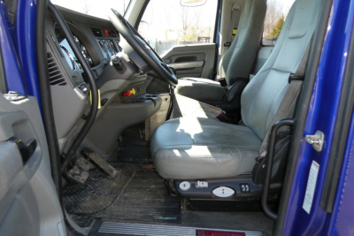 Kenworth T680 cab interior with gray seats and dashboard, driver seat controls, and open door showing entry step and pedals.