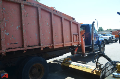 Truck chassis showing a large orange dump body and a blue International cab with a mounted loader attachment in the foreground.