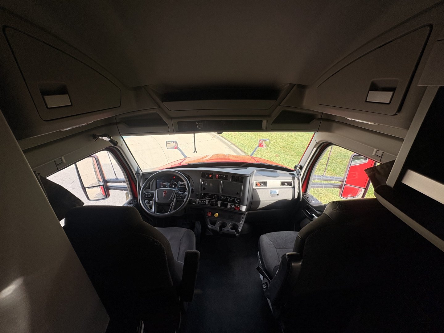 Kenworth T680 cab interior viewed from rear with dashboard and steering wheel visible, overhead storage cabinets, windows, and seating.