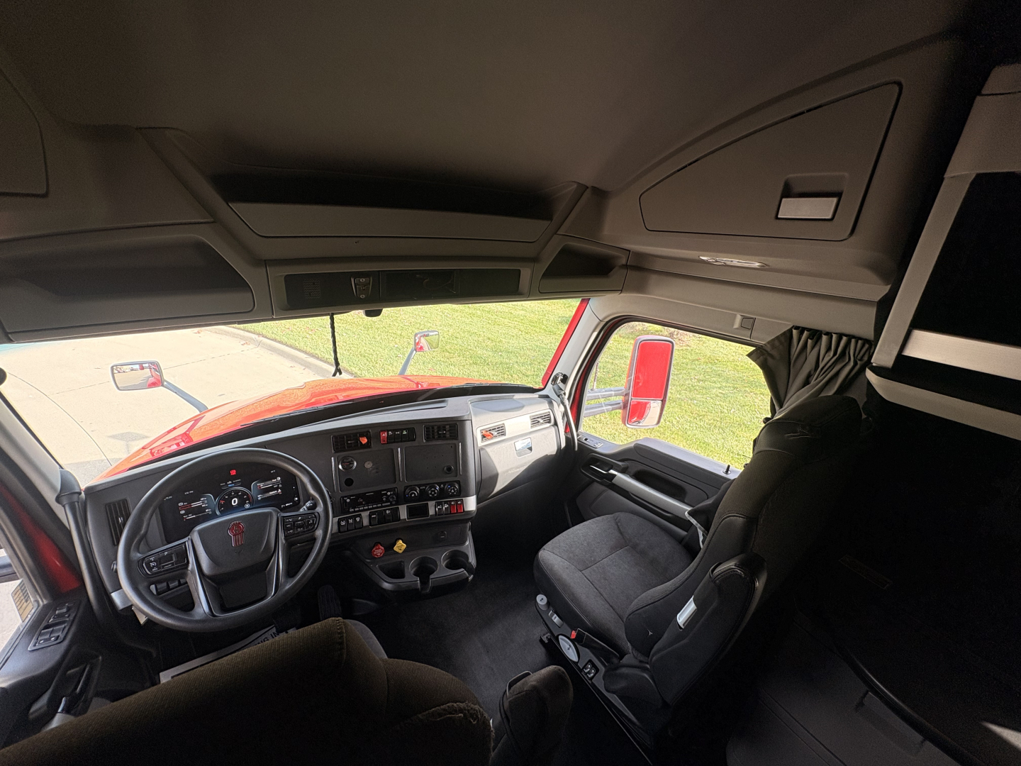 Kenworth T680 truck cab interior showing steering wheel dashboard and driver seat, with overhead storage compartments and window views.