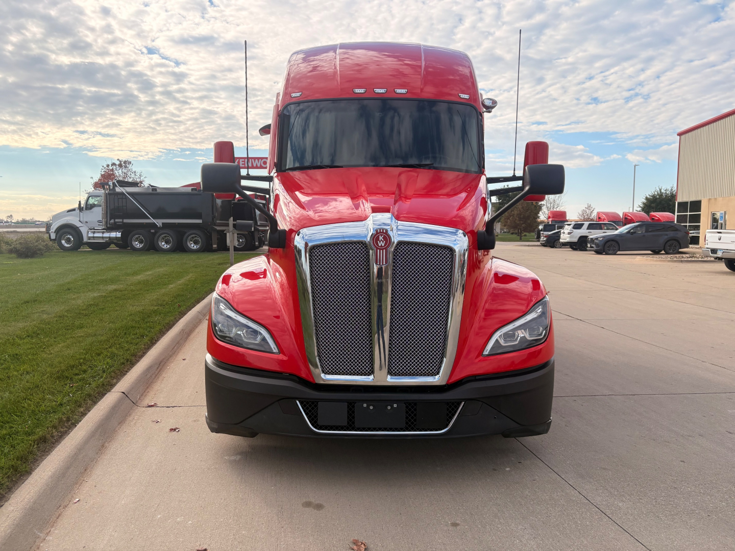 Front view of a red 2023 Kenworth T680 truck with black grille, large chrome centerpiece, black bumper, and side mirrors. Visible text includes Kenworth emblem and model styling on the grille area and no readable small labels.