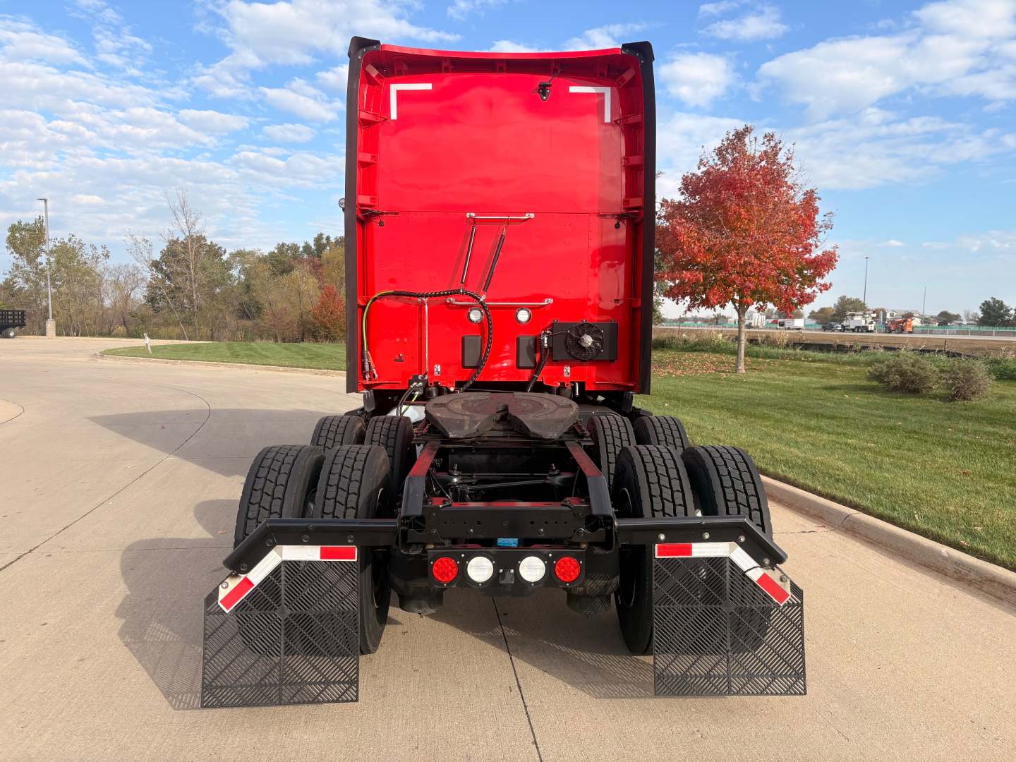 Kenworth T680 rear view showing fifth wheel, dual rear axles, mud flaps, and light bar with red cab; back of truck with red sleeper and black chassis.