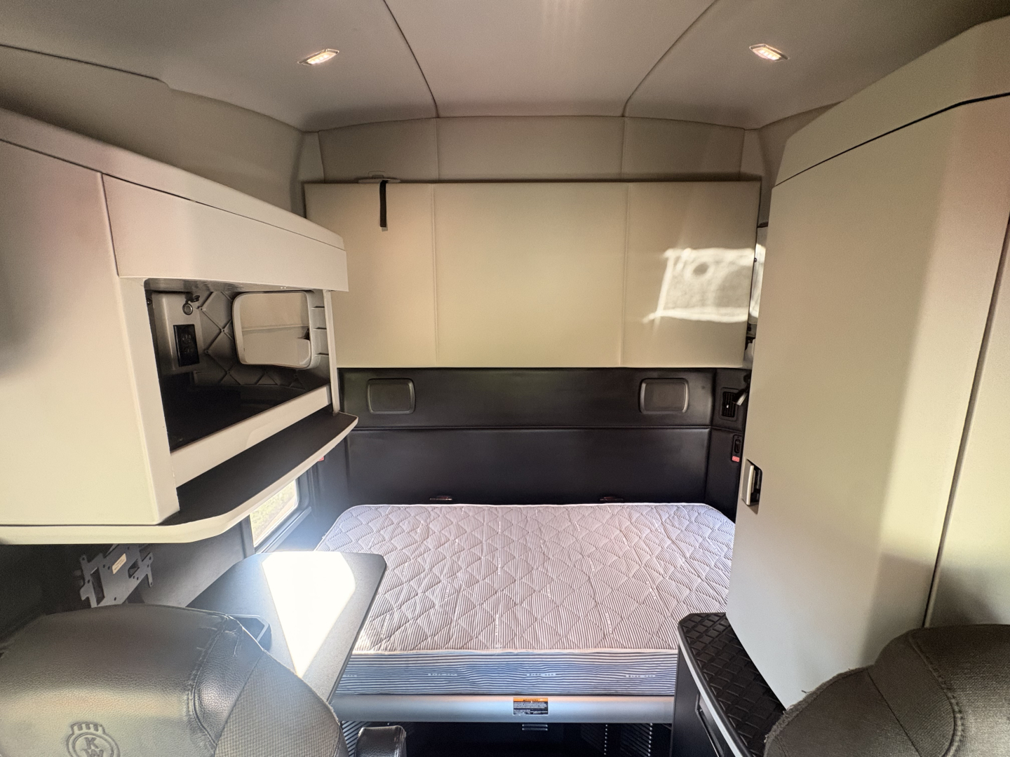 Kenworth T680 truck sleeper cab interior showing bed with mattress and storage cabinets.