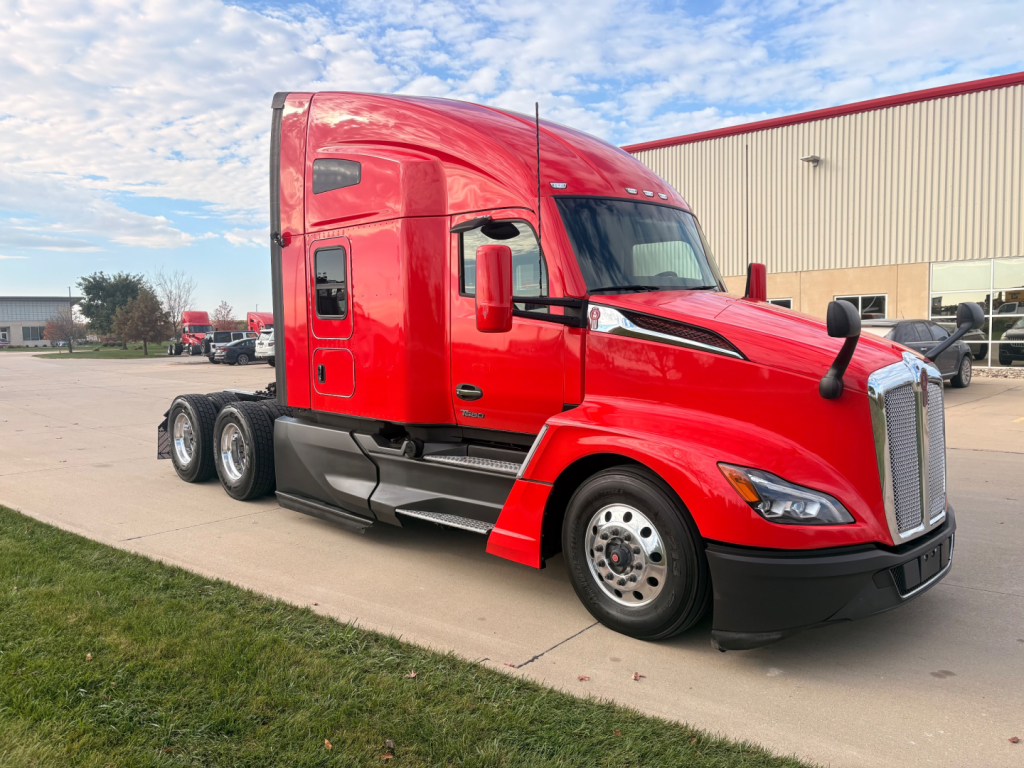 Kenworth T680 3/4 angled view red sleeper cab, single driver window, black bumper, dual rear axles, chrome grille, side steps, daytime sky