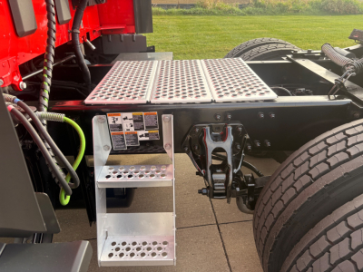 Kenworth T680 chassis area showing metal perforated steps, side platform, and wheel well with dual rear tires.