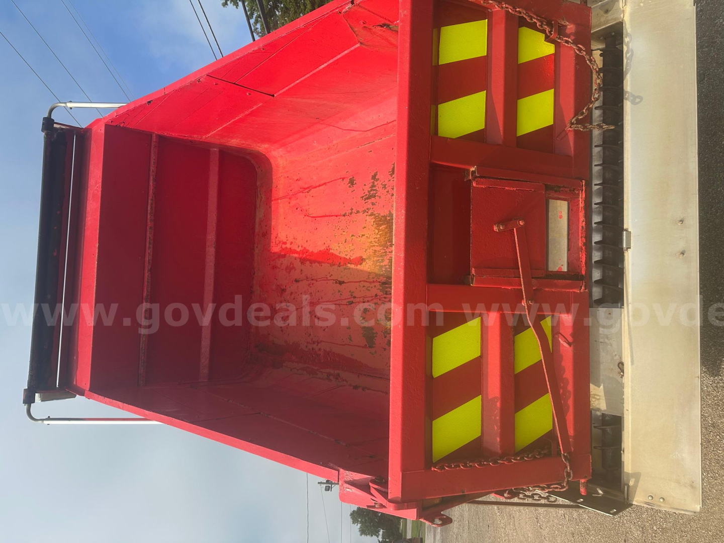Red dump truck bed with plow category, interior showing metal sides and reflective yellow stripes, side rails and tailgate, viewed from above.