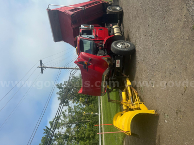 2008 International 7400 truck with a red cab and snow plow attachment in front, black wheels, yellow equipment on plow, side view.
