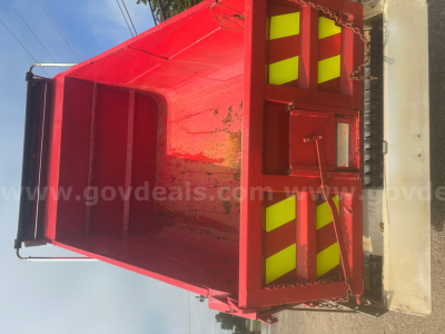 Red dump truck bed with plow category, interior showing metal sides and reflective yellow stripes, side rails and tailgate, viewed from above.