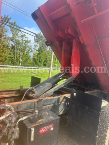 Truck chassis with a raised red dump bed showing hydraulic cylinder and metal components.