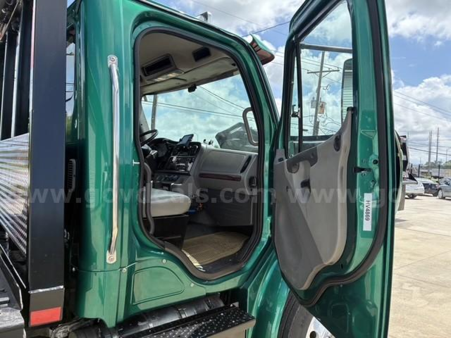 Cab of a green Freightliner M2 106 with open driver door, showing dashboard, steering wheel, and entry steps.