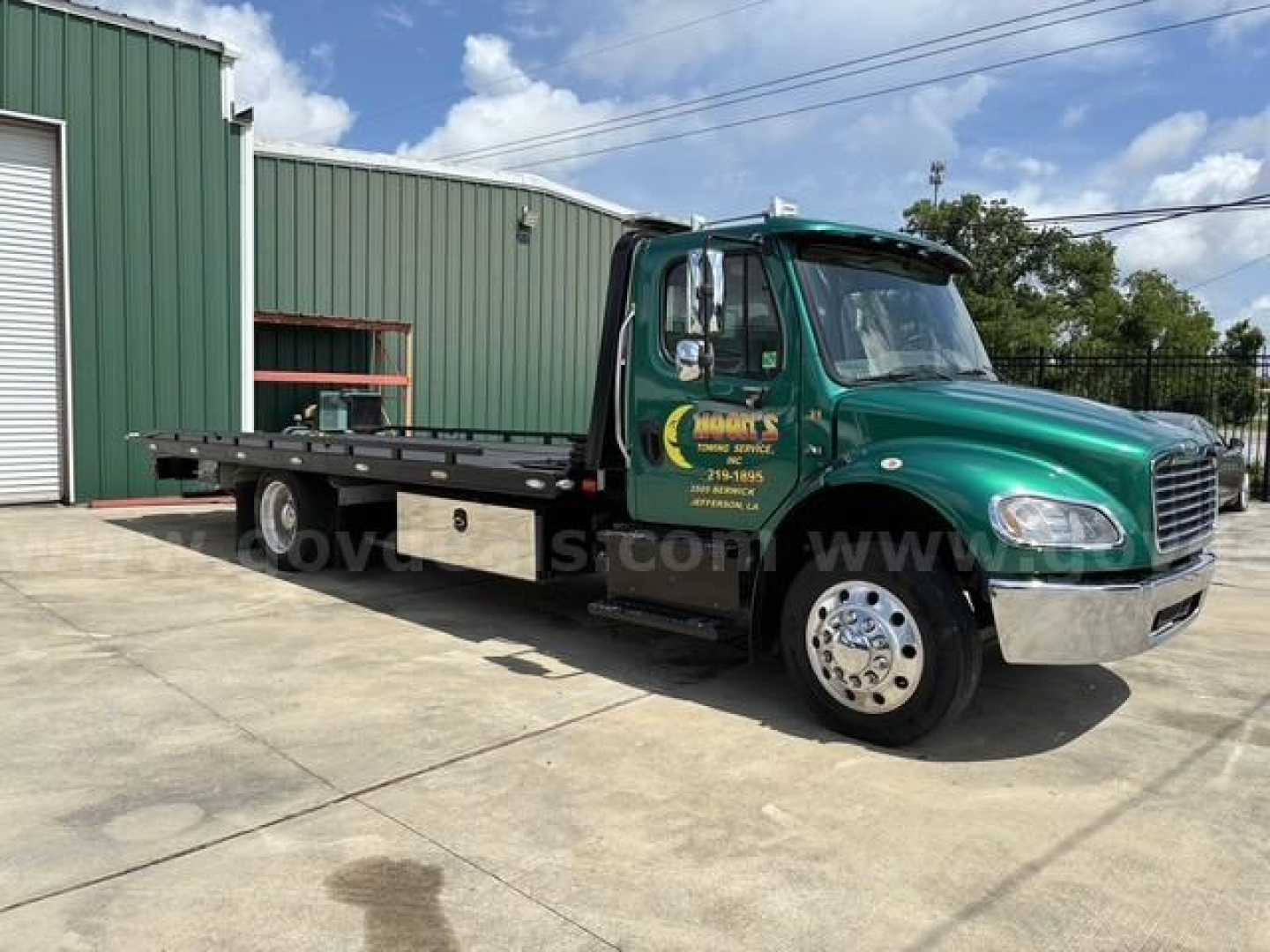 Truck cab and flatbed wrecker body showing Freightliner M2 106 sign on green cab and flatbed platform.