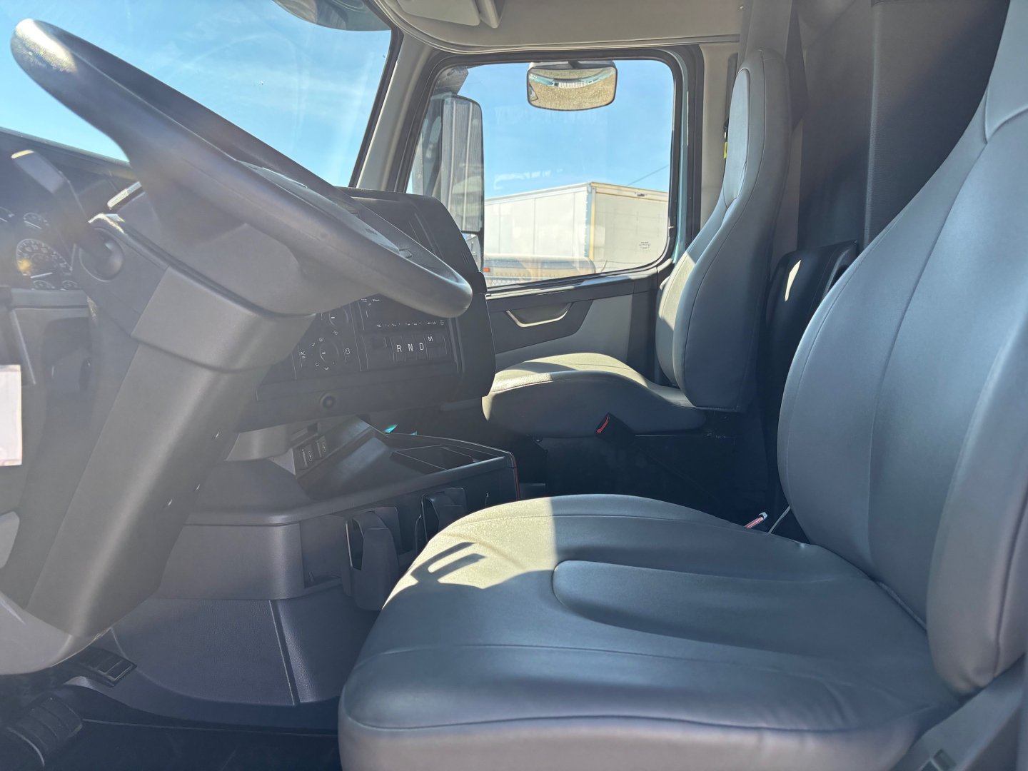 Volvo VNR interior cab view showing steering wheel, driver seat, and front passenger seat with dashboard and side window in sleeper truck.