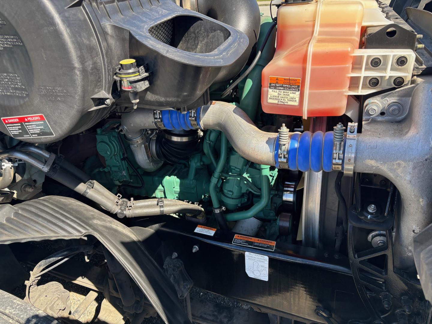 Volvo VNR64T660 engine bay showing coolant reservoir (orange cap), blue silicone hoses, green engine block, and black radiator support.