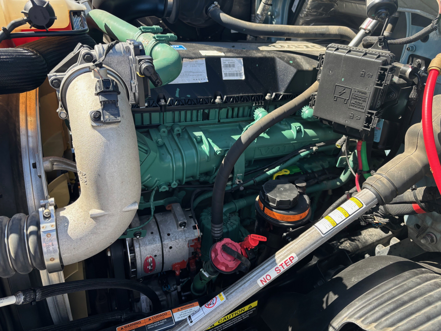 Volvo VNR64T660 engine bay showing green engine block, turbocharger piping, green hydraulic reservoir, and various hoses and wires.