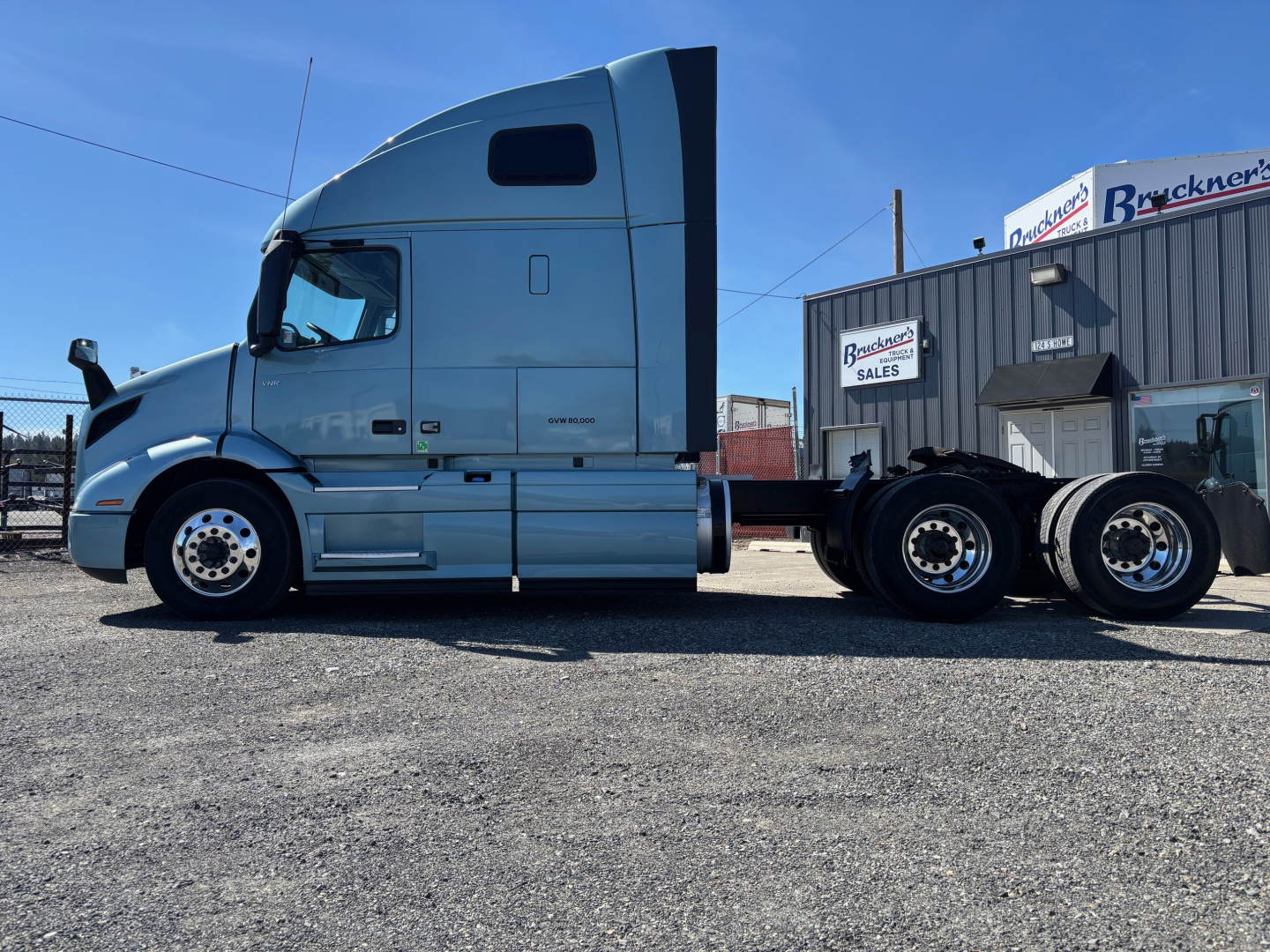 Truck tractor side view showing gray Volvo VNR cab and attached trailerless chassis with dual rear axles and fifth wheel, parked in lot.