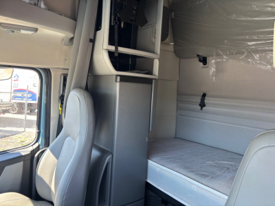 Truck cabin interior showing bunk bed area and passenger seat with overhead compartments and storage cabinets.