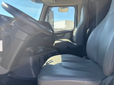 Volvo VNR interior cab view showing steering wheel, driver seat, and front passenger seat with dashboard and side window in sleeper truck.