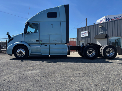 Truck tractor side view showing gray Volvo VNR cab and attached trailerless chassis with dual rear axles and fifth wheel, parked in lot.