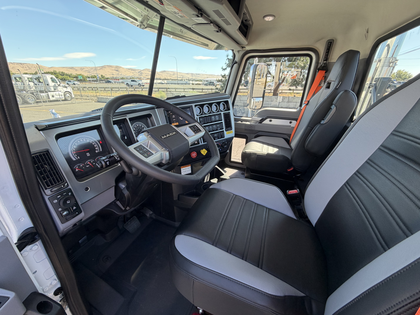 Mack PI84T truck cab interior showing steering wheel, dashboard, and driver’s seat with black and gray upholstery.