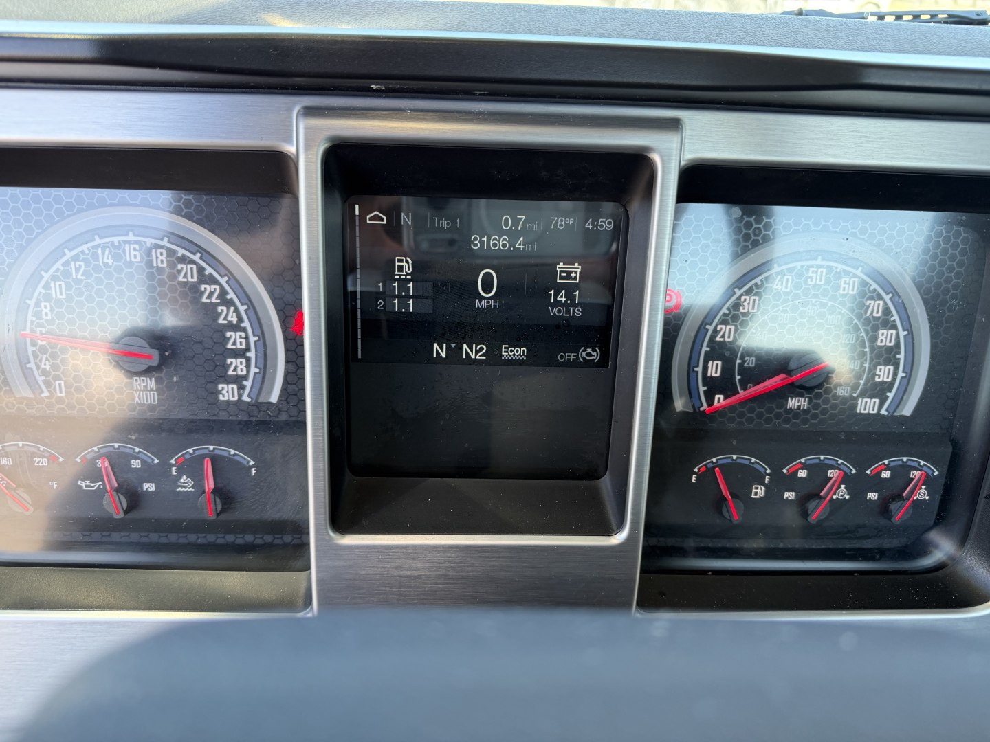 Dashboard display of a Mack PI84T truck showing digital instrument cluster with trip data, speedometer, and tachometer flanking a central screen.
