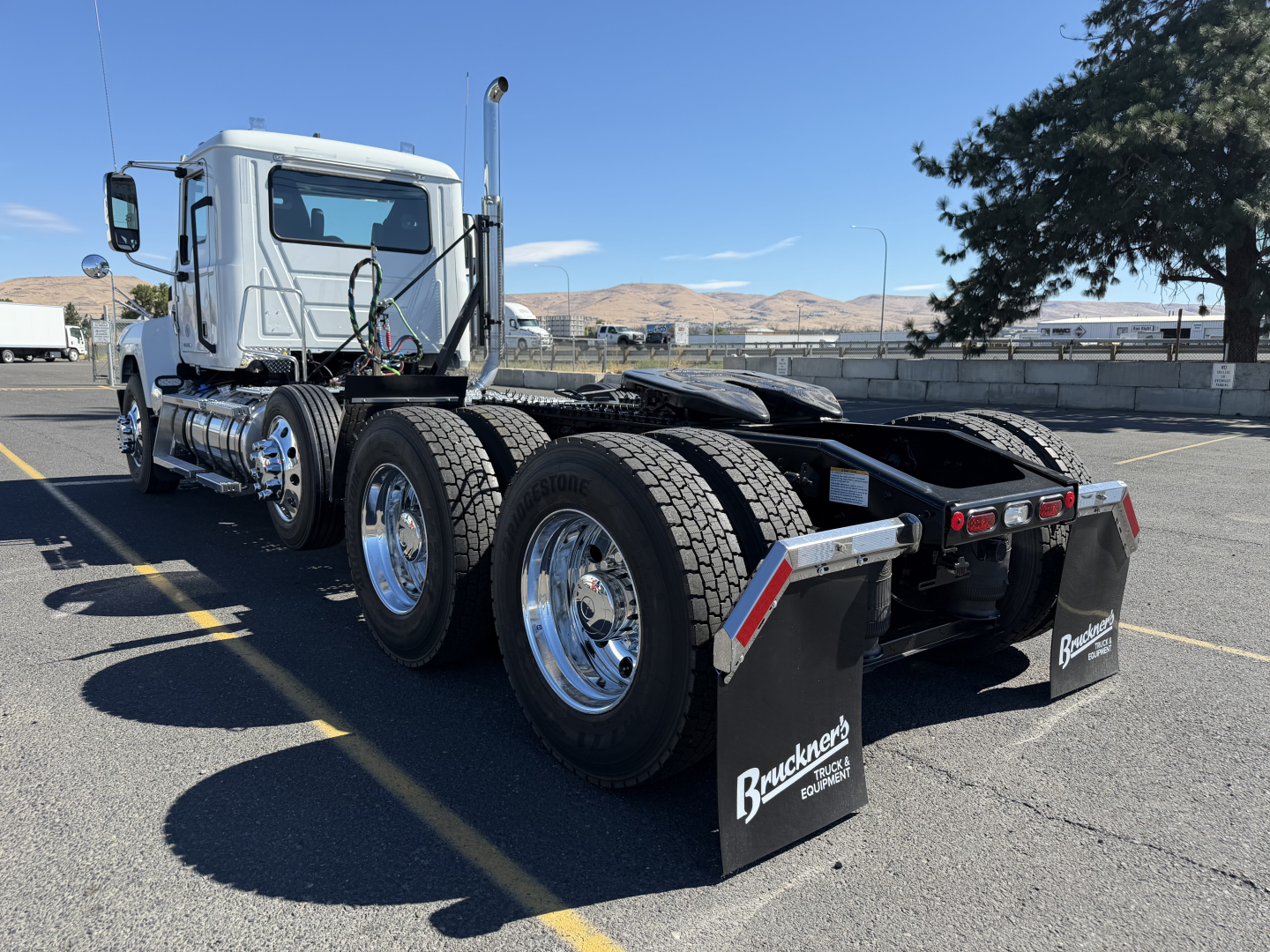 Mack PI84T conventional daycab tractor rear view showing dual rear axles, chrome wheels, and black mud flaps with Bruckner's logo.
