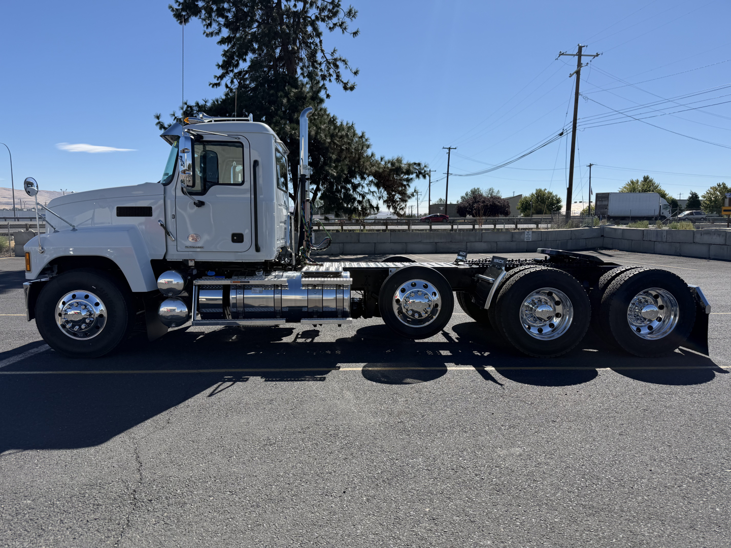 Side view of a white 2027 Mack PI84T conventional daycab tractor showing the cab, chrome fuel tanks, and dual rear axles.
