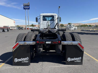 Truck rear view showing dual rear axles with mud flaps and Bruckner's Equipment branding, fuel/air lines visible, cab behind, bright day.