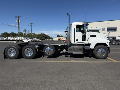 Truck chassis of a white 2027 Mack PI84T side view showing cab, dual rear axles, and exposed engine bay with chrome wheels.