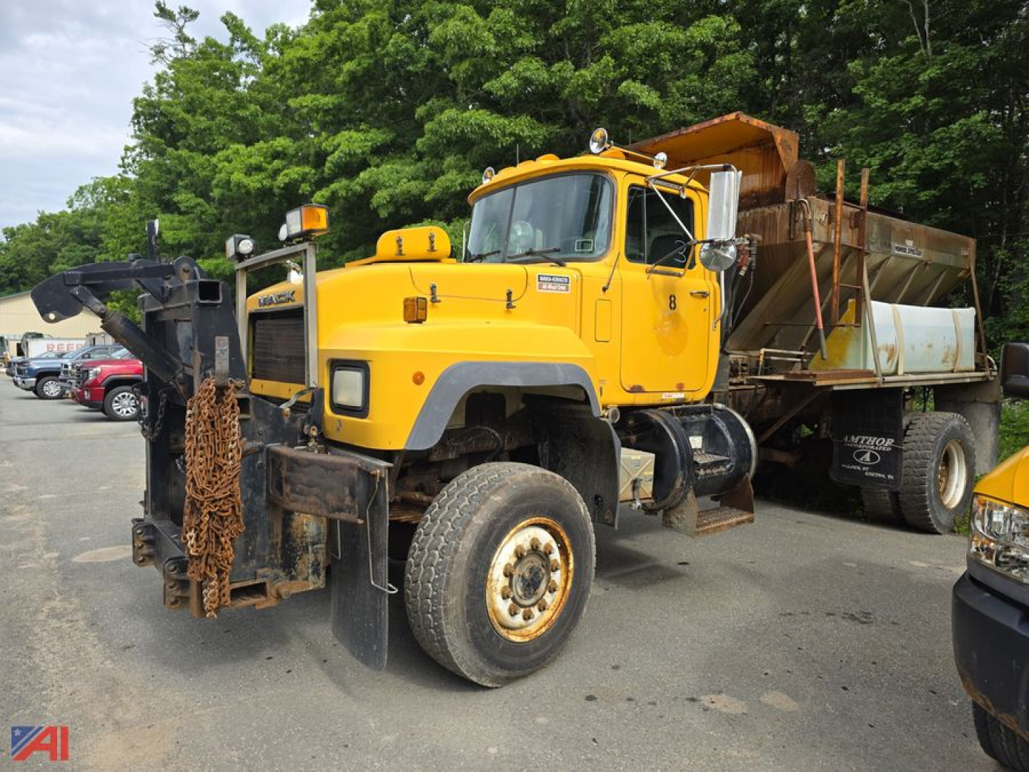Mack RD690P dump truck with sander body in yellow, front view showing heavy-duty tires and snow plow attachment; large hopper at rear.
