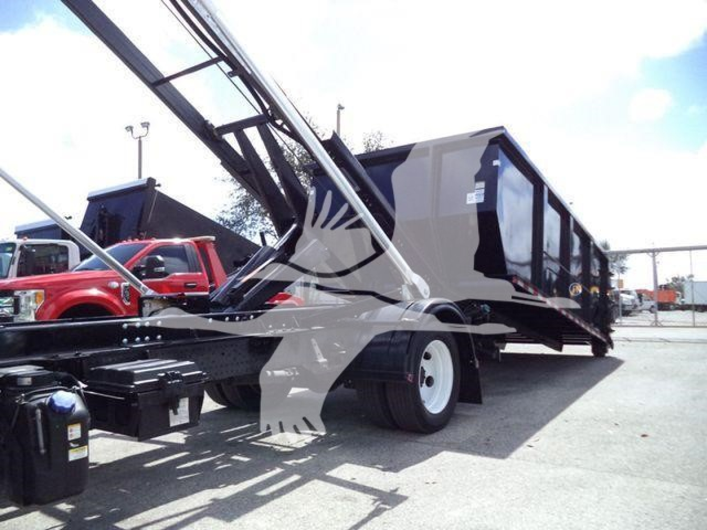 Isuzu NPR (2021) rollover truck with long black dump bed and hydraulic arm, side view showing rear wheels and crane mechanism.