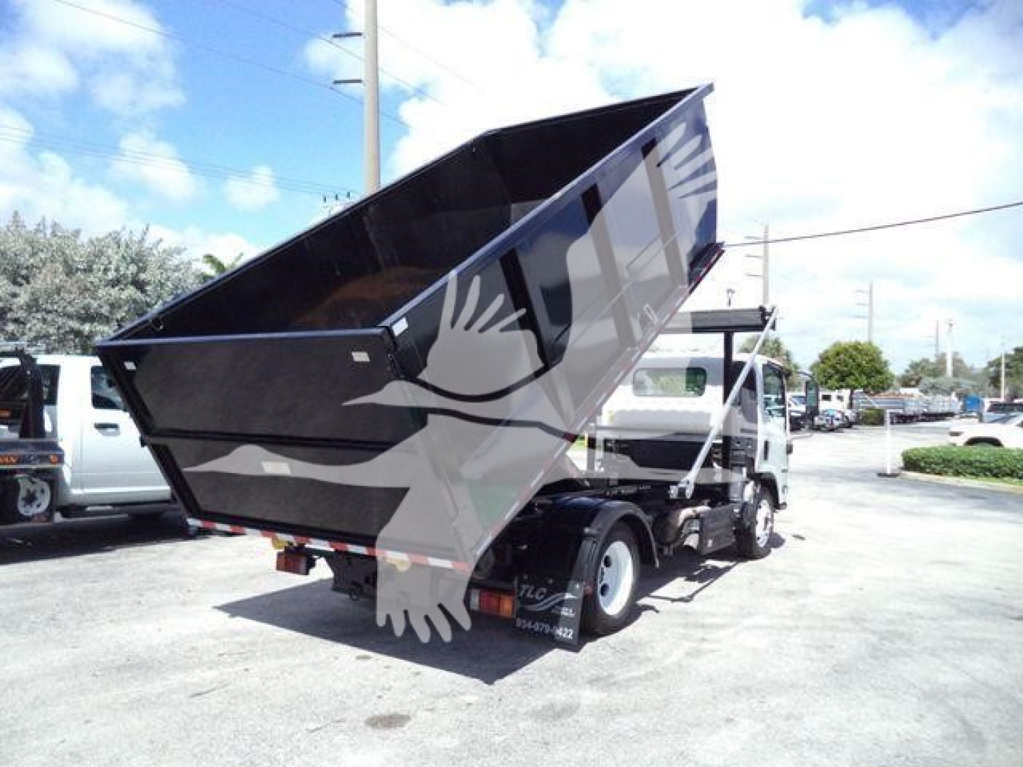 Isuzu NPR/NRR medium-duty dump truck with raised dump bed in a vehicle lot, side view showing rugged rear mechanism and hydraulic components.