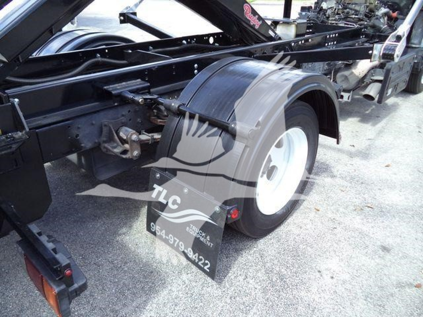 Isuzu NPRR truck rear wheel seen from side with TLC logo mudflap and chassis components visible.